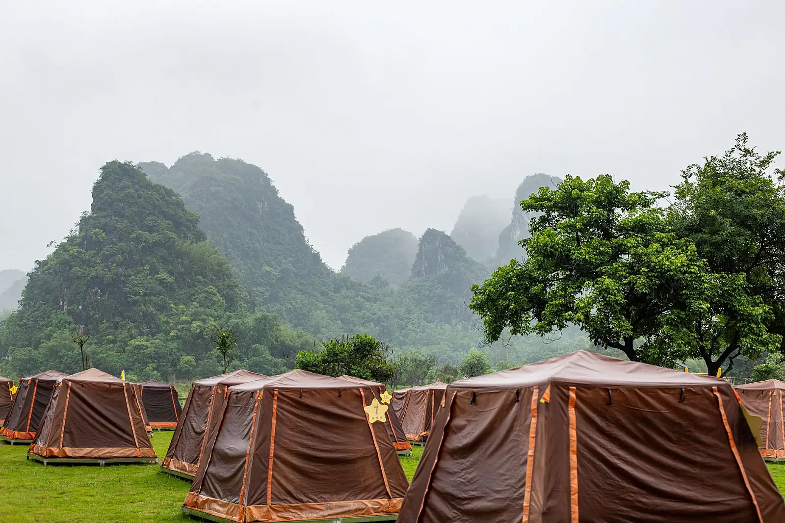 Tents in a lush green campsite with scenic mountains in the background on a misty summer day.